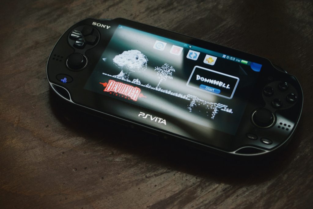 Une PlayStation Vita posé sur un support en bois. Le jeu Downwell (Moppin) est sur l'écran d'accueil.